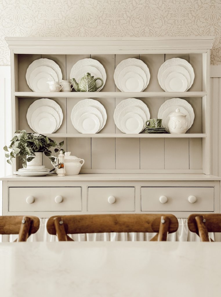 Wooden hutch in the kitchen decorated with white plates, cabbage ware dishes, and greenery.
