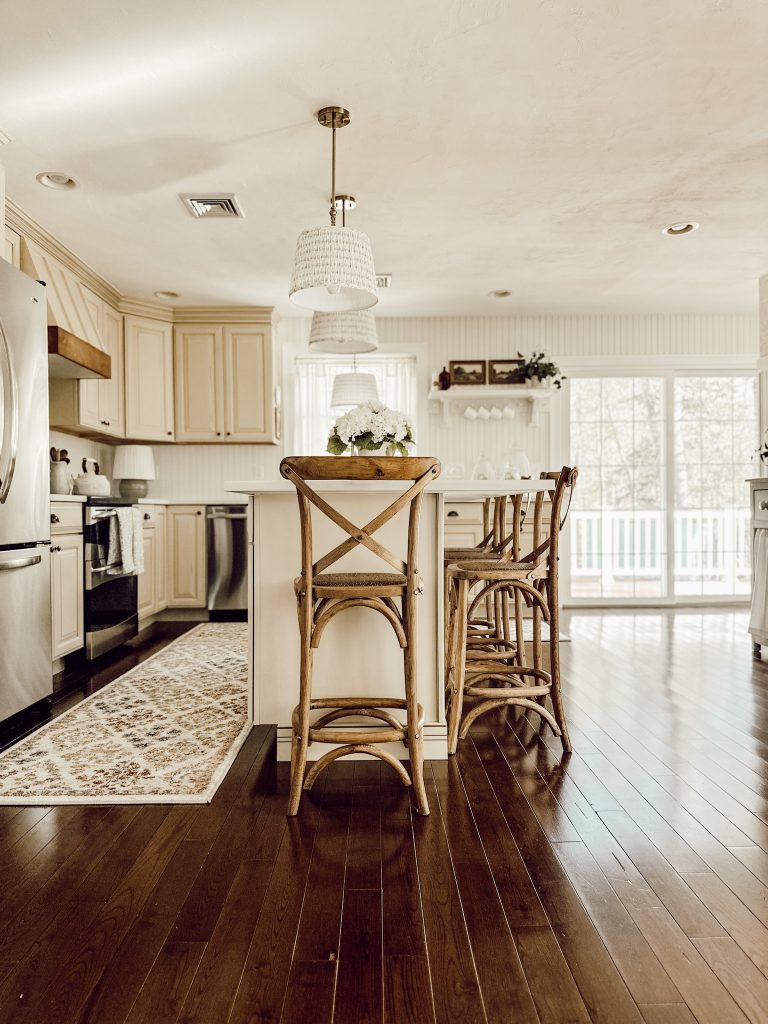 Country cottage kitchen style with wooden bar stools, wood floor, area rugs, shaded pendant lights, and seasonal accents.