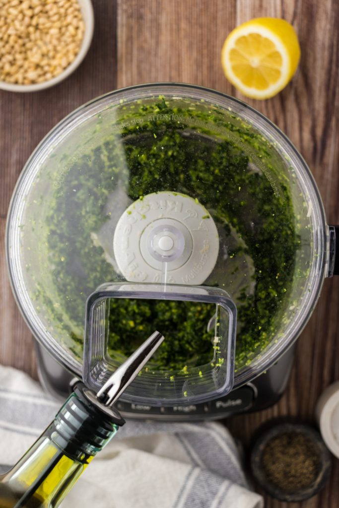 Pouring in a steady stream of extra virgin olive oil into the homemade pesto.