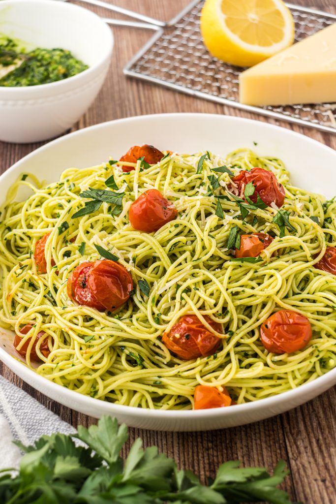 Bowl on angel hair parmesan pesto pasta on a wooden table with roasted tomatoes.