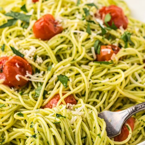 A large bowl of angel hair pesto pasta with roasted tomatoes and grated parmesan cheese.