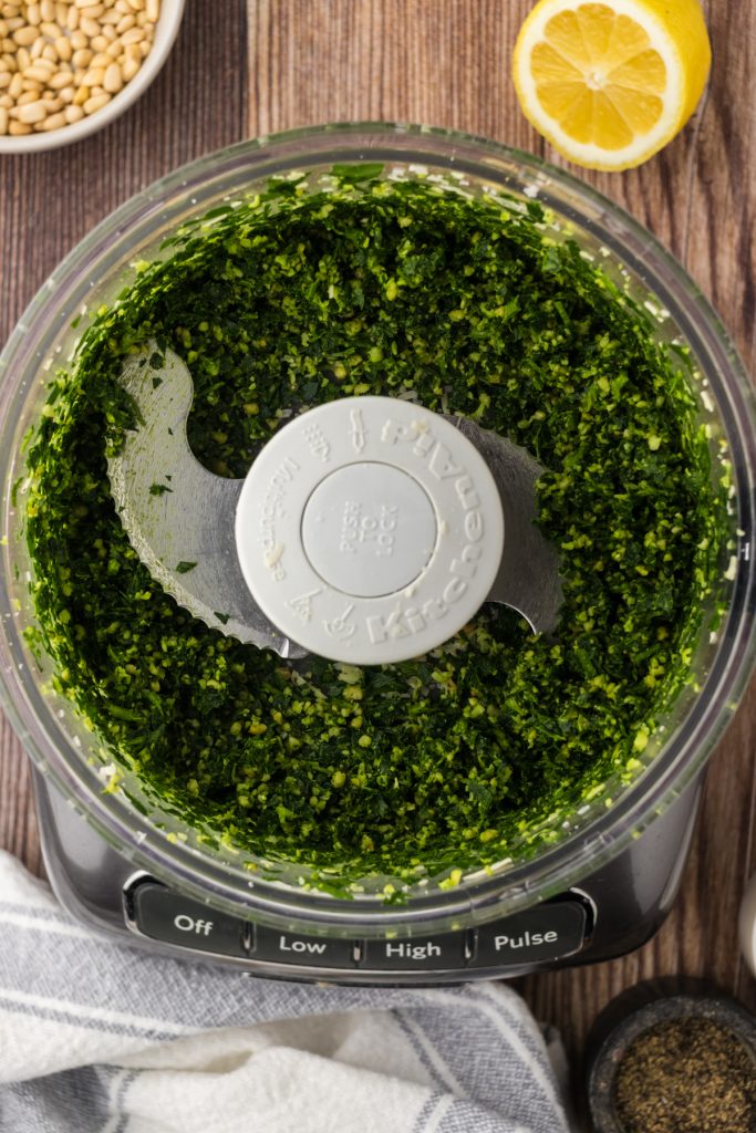 Blended pesto ingredients in the bottom of the bowl of the food processor.