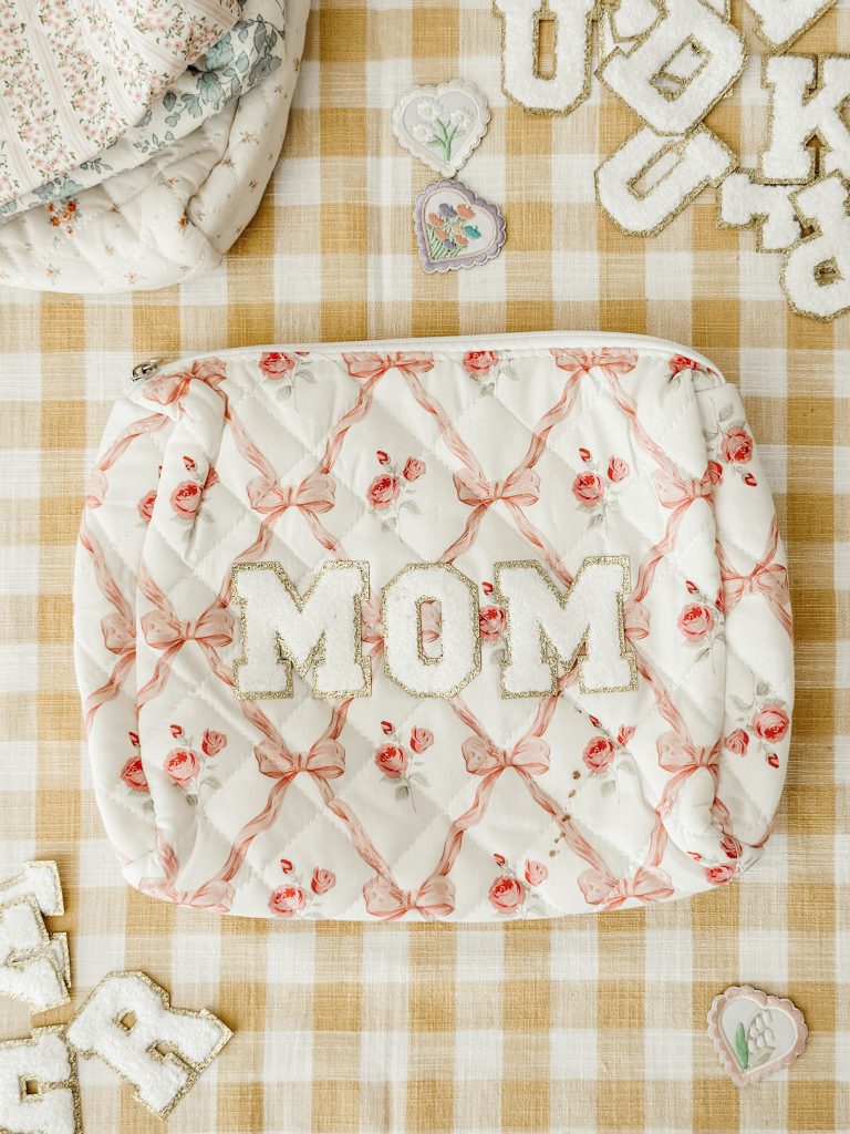 Customized floral quilted makeup bag with the iron-on letters MOM on a yellow and white gingham tablecloth.