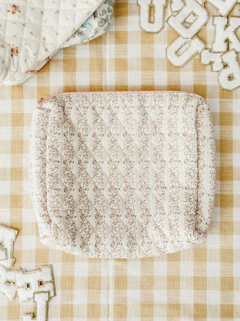 Floral quilted pouch on a yellow and white gingham tablecloth with iron-on patches scattered about.