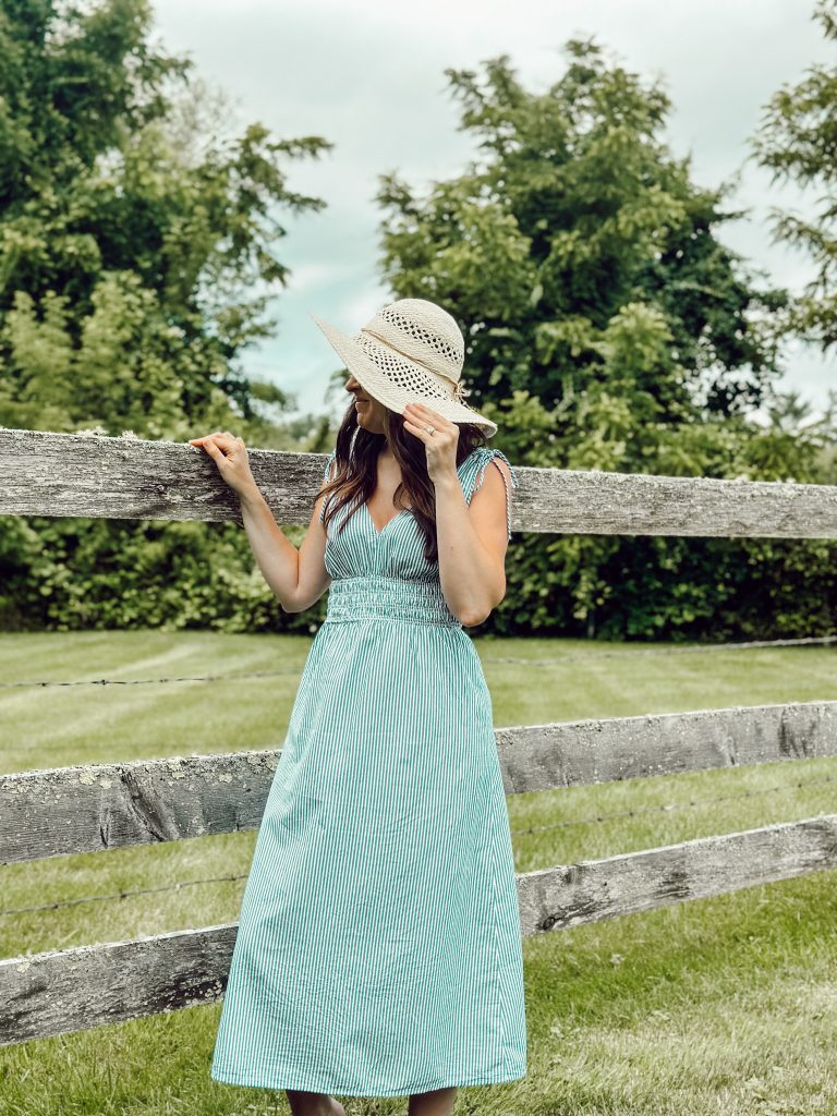Heidi outside in a straw hat and blue striped flowing dress enjoying the summer season tomato girl style.