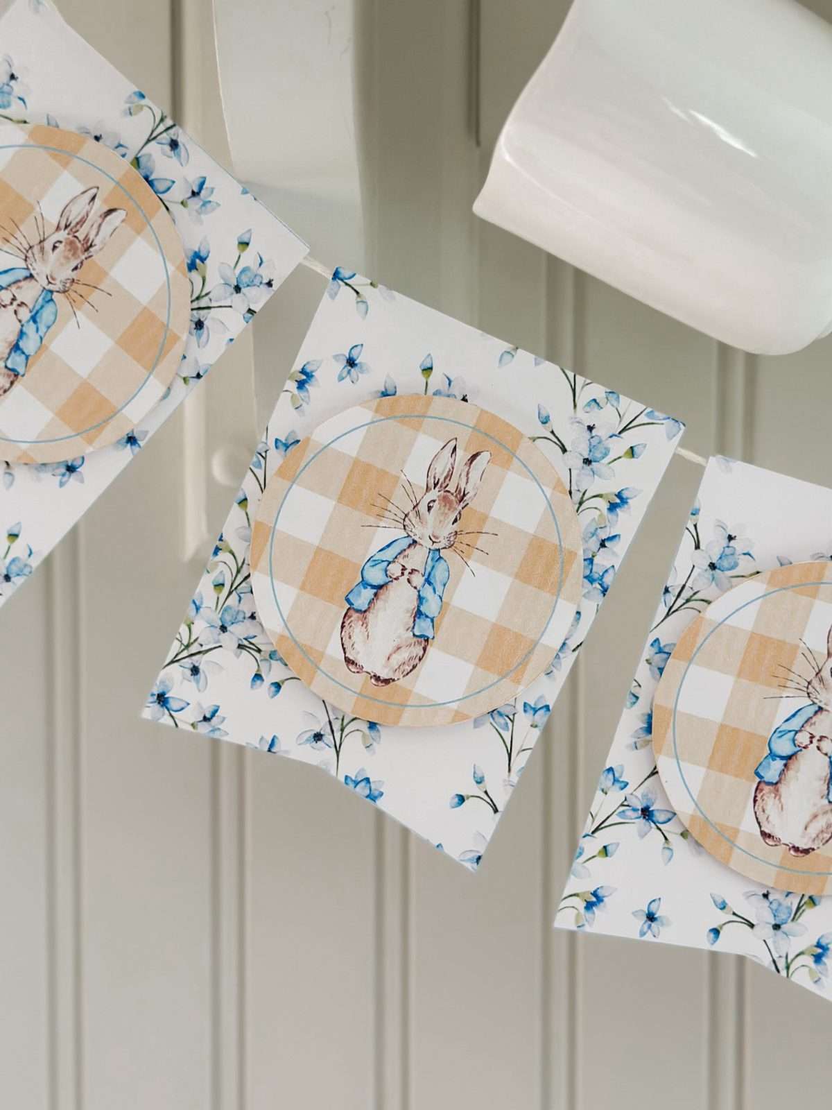 Peter Rabbit garland hanging on peg hooks in the kitchen with white coffee mugs.