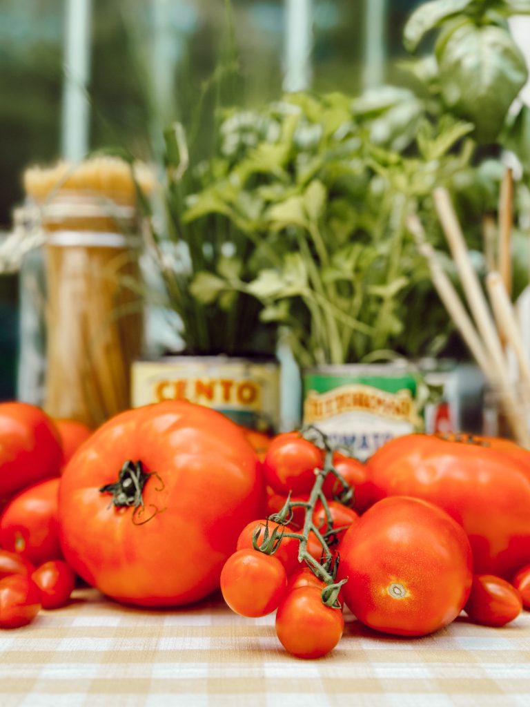 Red ripe tomatoes on an outdoor table with a yellow gingham tablecloth to romanticize a tomato girl summer.