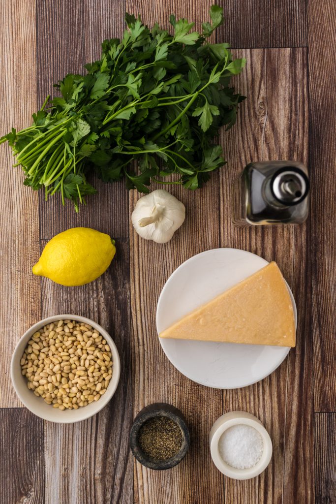 The simple ingredients for parsley pesto sauce include bunch of parsley, lemon juice, parmesan cheese, garlic cloves, extra virgin olive oil, pine nuts, and salt & pepper.