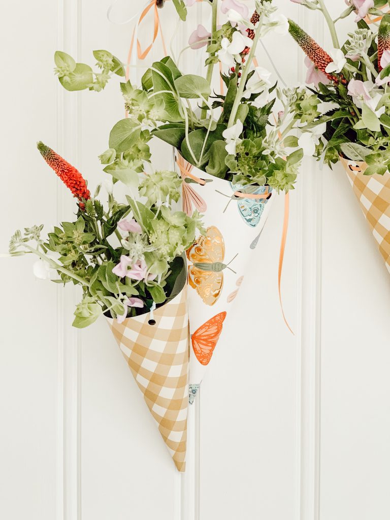 Simple May Day baskets with fresh spring flowers and paper cones hanging on hooks.