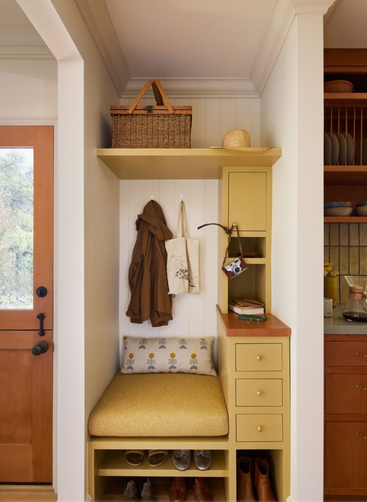 Small entryway with yellow built-in seating, accent pillow, and a basket on a shelf.