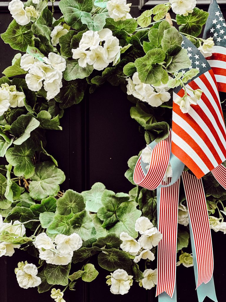DIY Fourth of July wreath for summer on a black front door with small American flags and red striped ribbon and blue ribbon.
