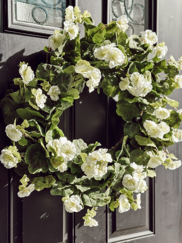 Faux floral wreath with flowers and greenery on front door of entryway. 