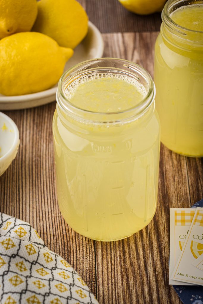 Fresh homemade lemonade concentrate in a mason jar with a bowl of fresh lemons and a kitchen towel.