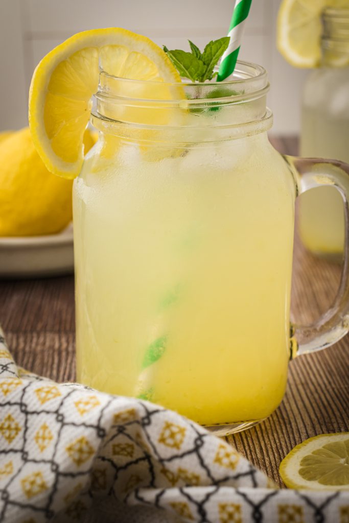 A glass of homemade lemonade using lemonade concentrate. Glass is garnished with a lemon slice and sprig of fresh mint.