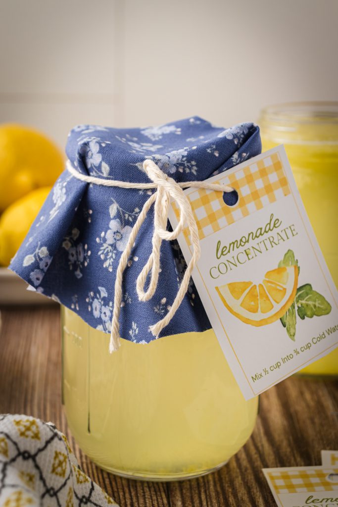 A mason jar filled with homemade lemonade concentrate with blue fabric on the lid tied with kitchen twine and a gift tag for gifting to friends and family.
