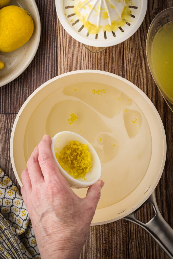 Adding lemon zest to the simple syrup in a medium saucepan to make homemade lemonade concentrate.