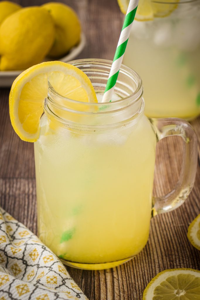 Mason jars of homemade lemonade with a paper straw and lemon slice on a wooden table.