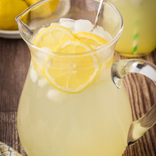 Glass pitcher of fresh homemade lemonade on a wooden kitchen countertop.