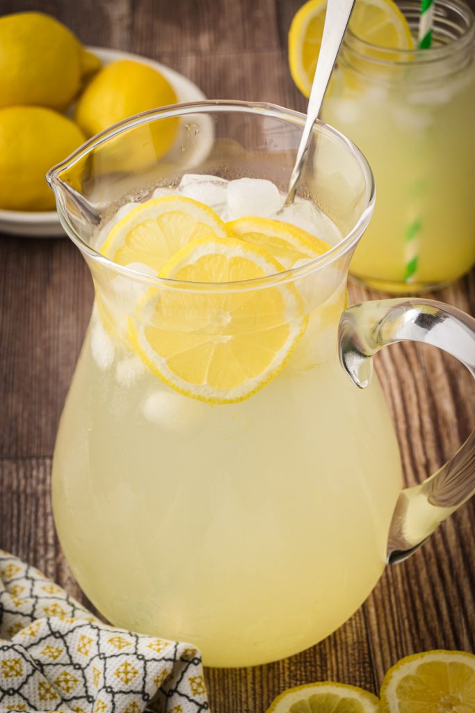 Glass pitcher of fresh homemade lemonade on a wooden kitchen countertop.