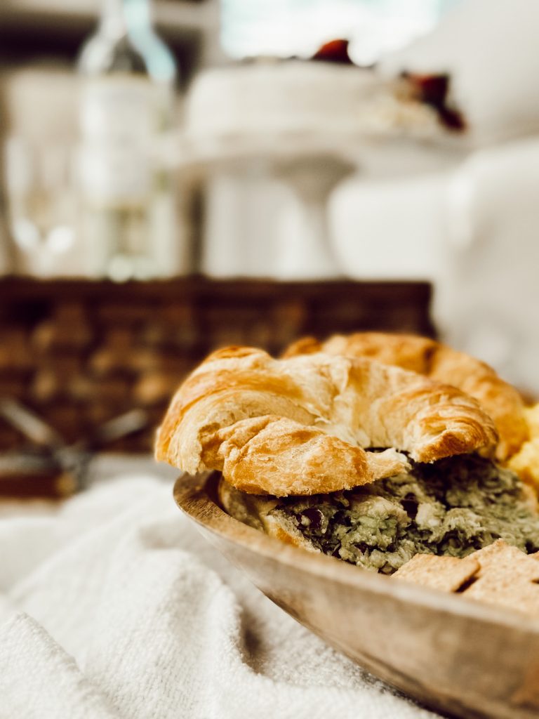 Avocado chicken salad on a buttery croissant roll on a charcuterie board for a picnic.