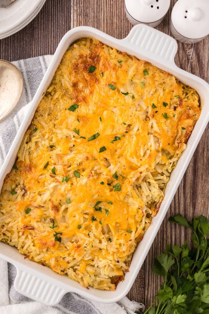 Baked hashbrown casserole in a white casserole dish on a wooden table ready for serving.