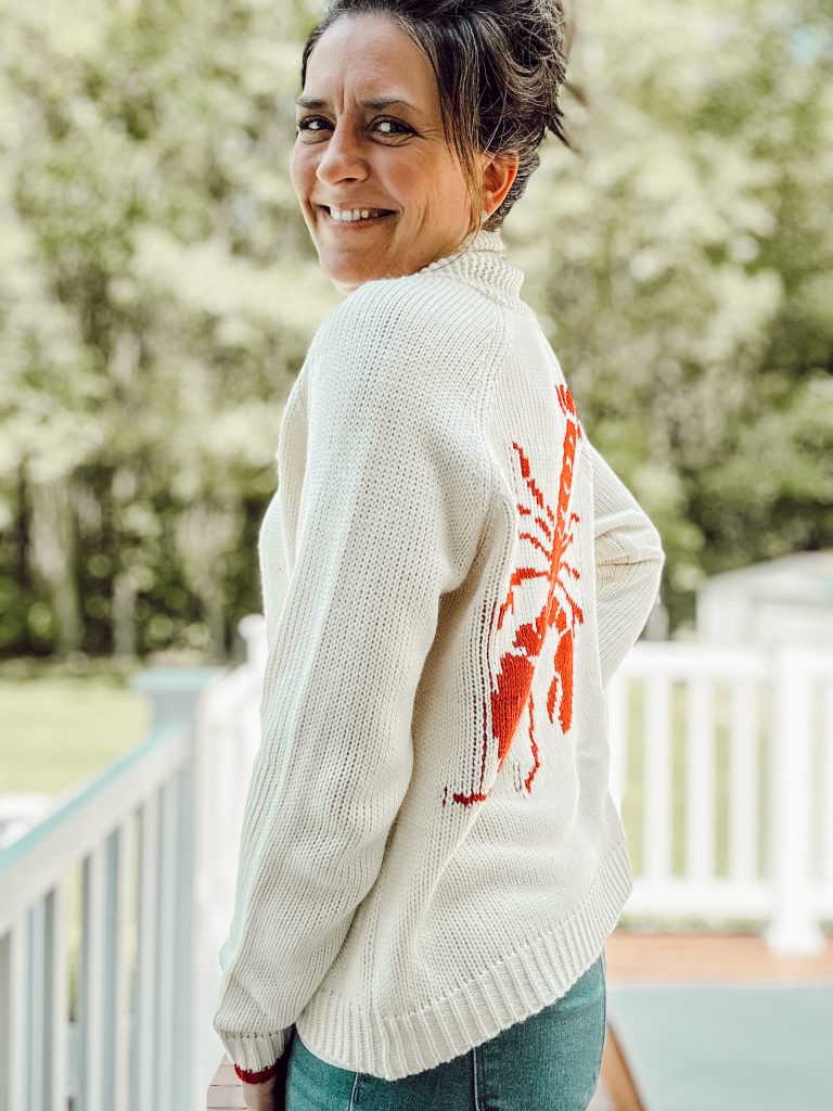 Heidi of Eleanor Rose Home in a shawl collar knit cardigan with a lobster on the back sharing the fisherman aesthetic trend.