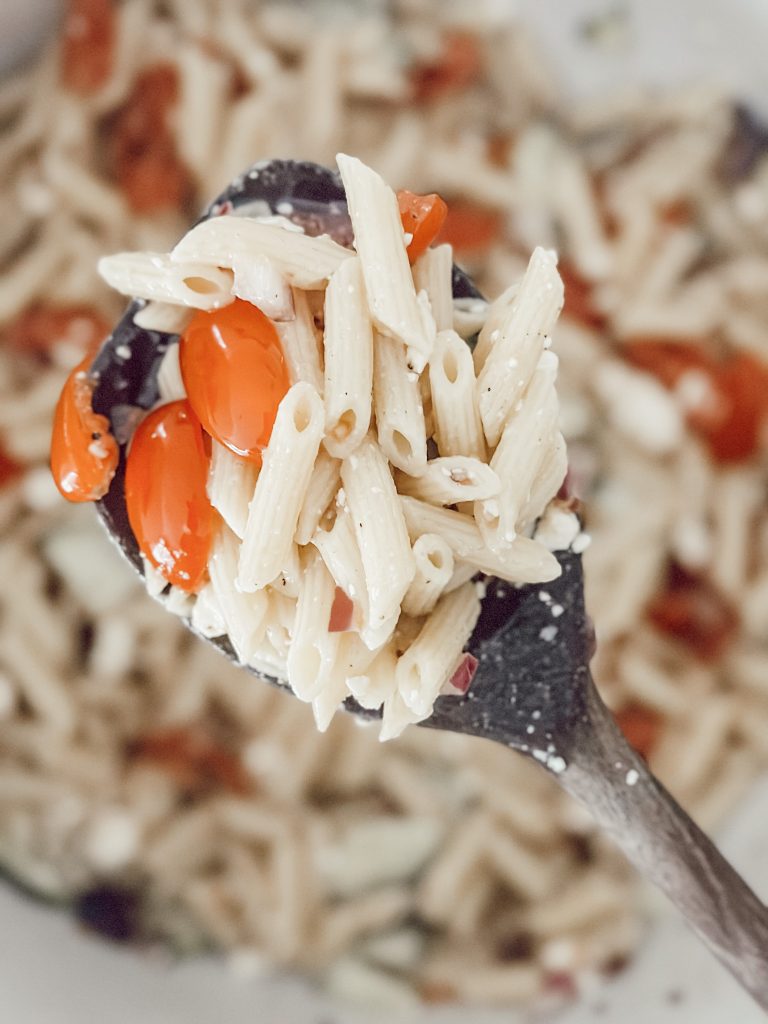 Cold penne pasta salad with feta cheese and grape tomatoes served in a large bowl.