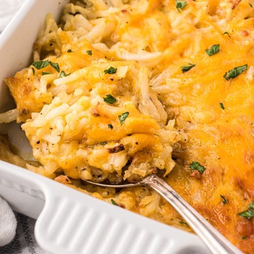 Creamy hash brown casserole recipe in a white baking dish with a silver serving spoon.