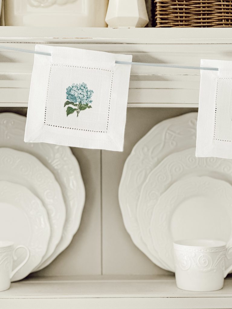 DIY fabric garland hanging on hutch made with fabric coasters and blue satin ribbon.