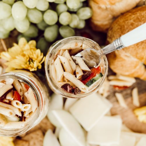 Pasta salad with homemade dressing in a mason jar for serving at a summer BBQ made with tender penne pasta, fresh tomatoes, cucumbers, olives, onion, and creamy feta.