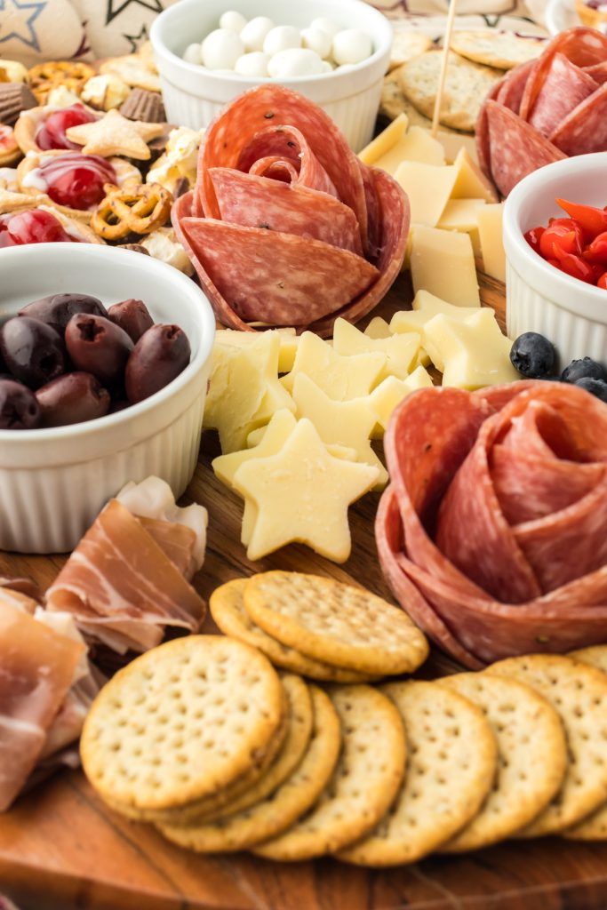 July 4th grazing board for potluck parties or summer barbecues with crackers, savory meats, olives, cheeses, and sweet treats.
