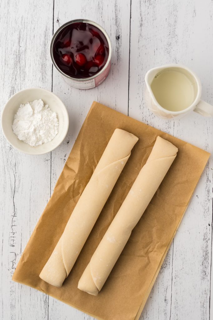 The simple ingredients you can find at the grocery store to make mini cherry pies include pre-made pie crusts, cherry pie filling, powdered sugar, and milk.