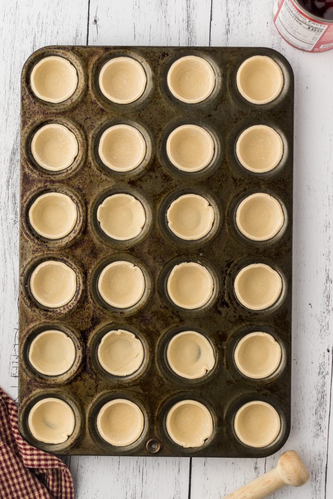 Pie crust in the muffin pan ready for baking in the oven to make mini cherry pies.