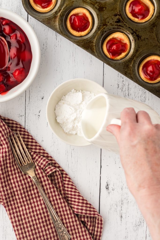 Pouring milk into powdered sugar to make the glaze for the top of the mini cherry pies.