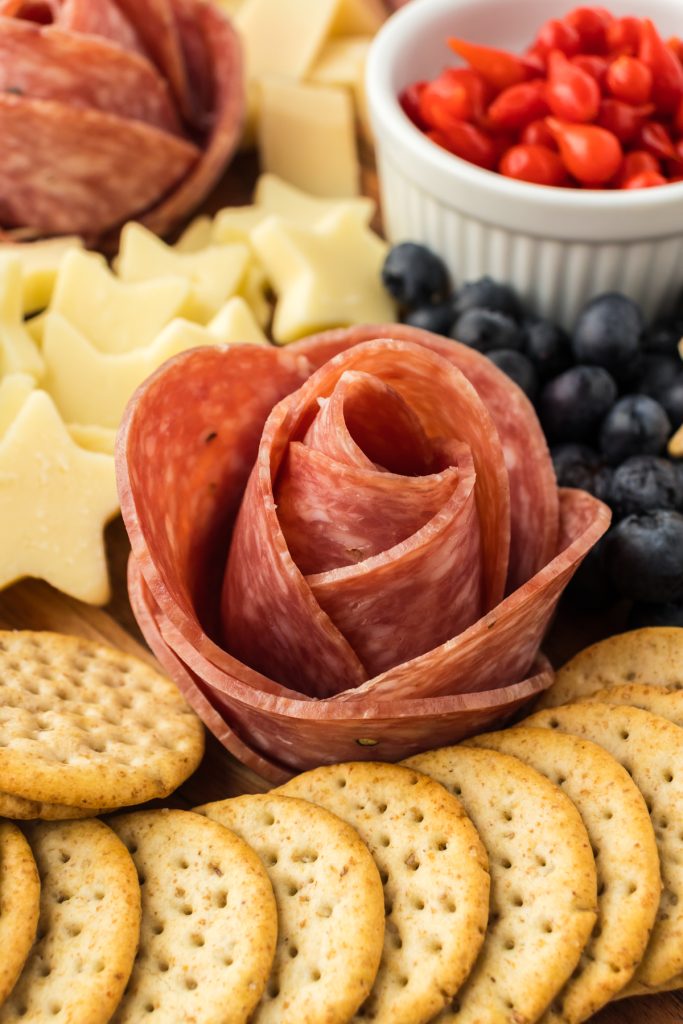Salami Rosete on patriotic snack board along with crackers, cheese, fresh blueberries, and red peppers.