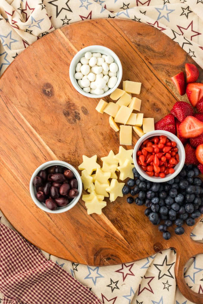 The first step in building a charcuterie board is adding small bowls to the board to hold messy ingredients like olives or red peppers.