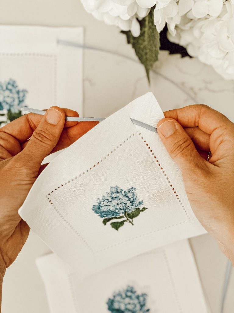 Threading blue satin ribbon through white hydrangea printed coasters.