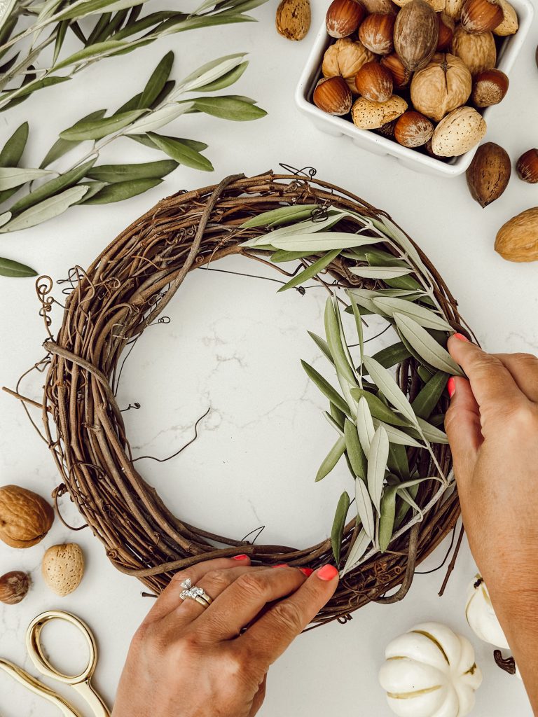 Placing an olive branch on the top of the grapevine wreath to start the candle ring.
