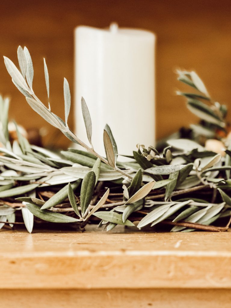 DIY fall candle ring with olive branches, nuts, white pumpkin, and a pillar candle in the middle.