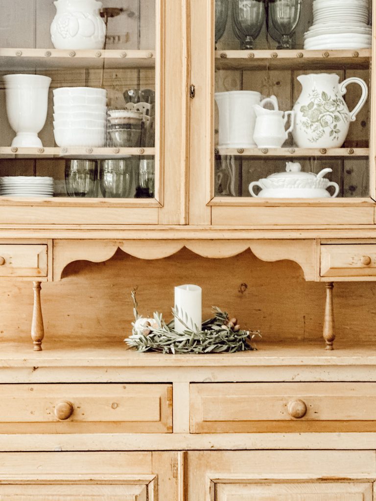 Decorated scrubbed pine hutch in the kitchen with dinnerware, glasses, and ironstone pitchers.