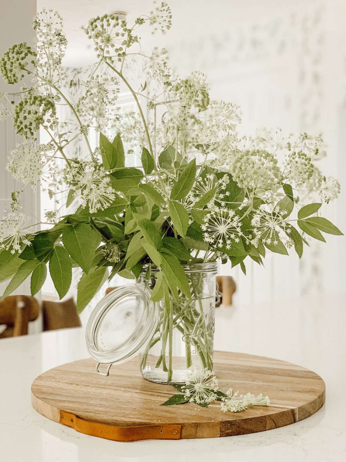 Mason jar on a wooden tray on the kitchen counter filled with weeds from the yard.