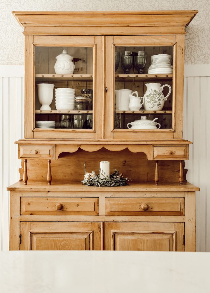 Scrubbed pine kitchen hutch decorated with white plates, green glasses, and vintage pieces to create a cozy cottage kitchen. 