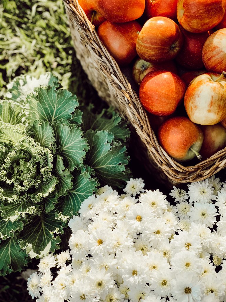 Fall decorations for outdoor entertaining include fresh apples in a woven basket, kale, and mums.