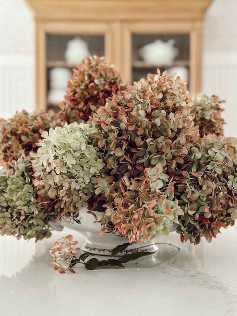 Hydrangea flowers in a centerpiece on kitchen island countertop with pine hutch behind it.