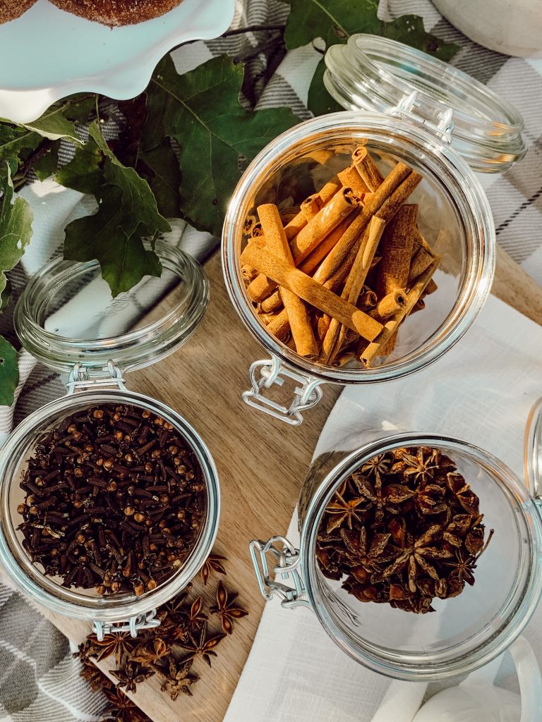 Glass mason jars filled with whole cinnamon sticks, star anise, and whole cloves.