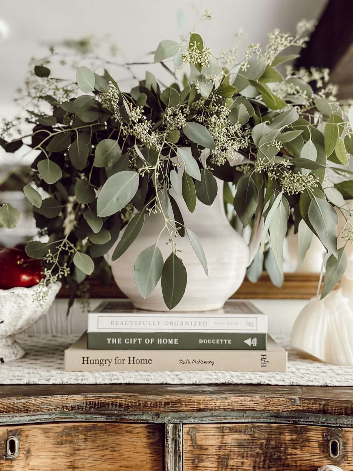 Weekly Wednesday Wish List #219 Eleanor Rose Home vase filled with seeded eucalyptus on a stack of books with a bowl of red apples.