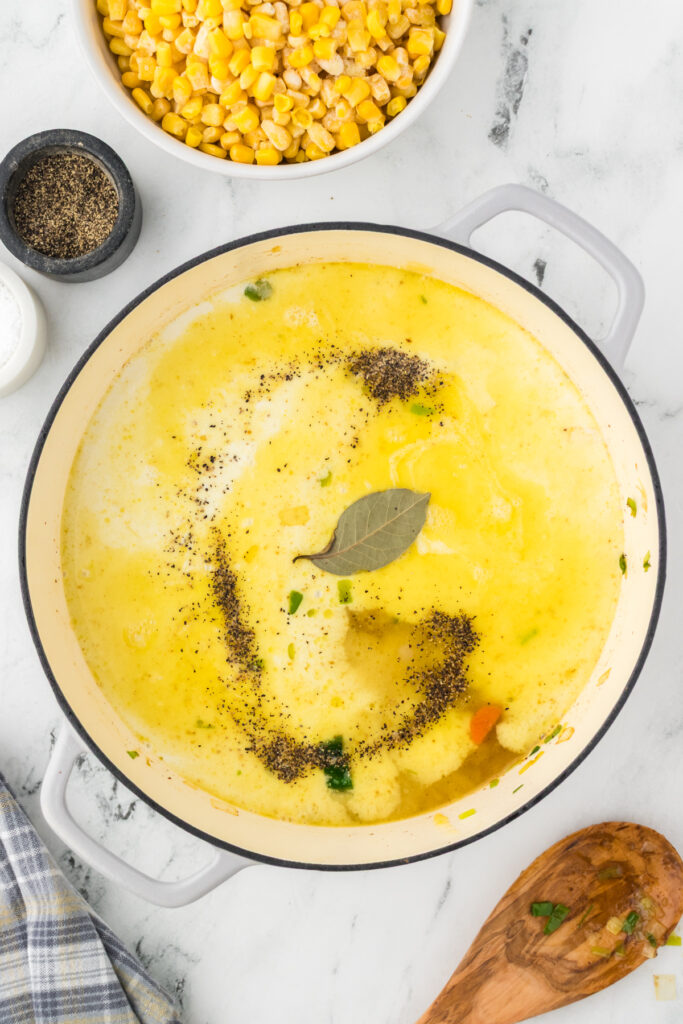 Add a bay leaf, kosher salt, and black pepper to the creamy base of the corn soup.
