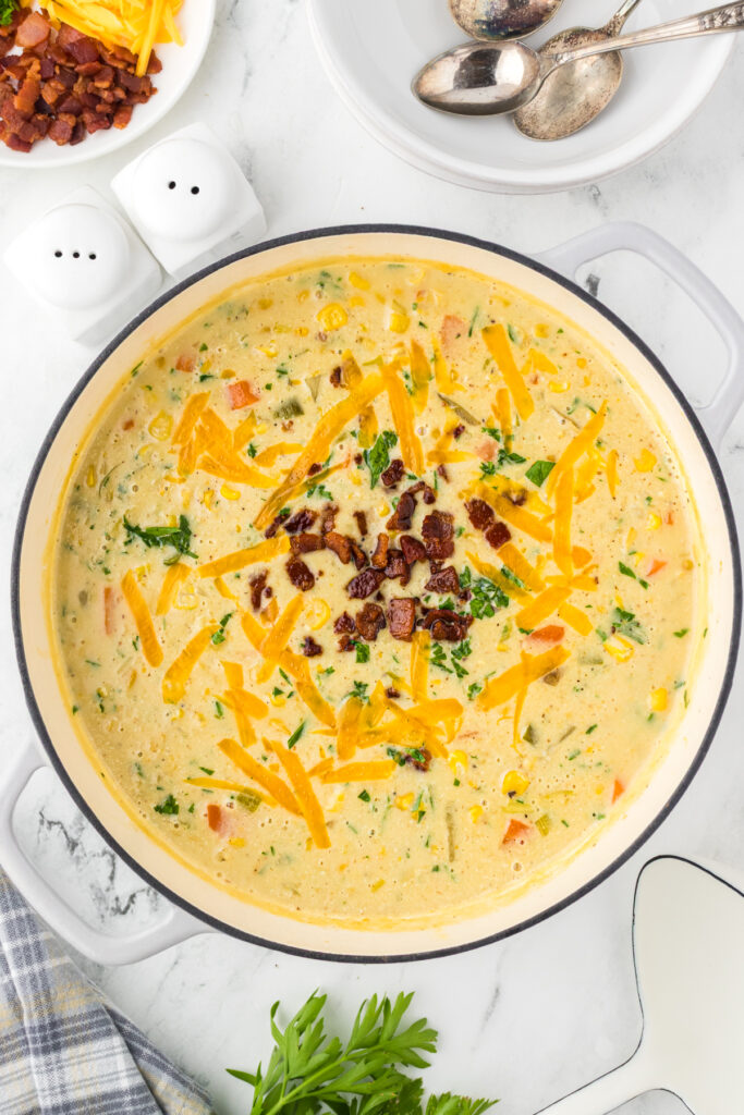 Dutch oven of easy creamy corn chowder topped with shredded cheese, chopped bacon, and fresh parsley.