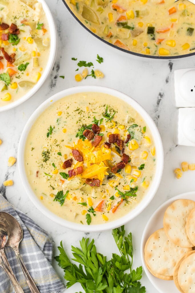 A bowl of easy creamy corn chowder garnishes with chopped bacon, shredded cheddar cheese, and chopped parsley.