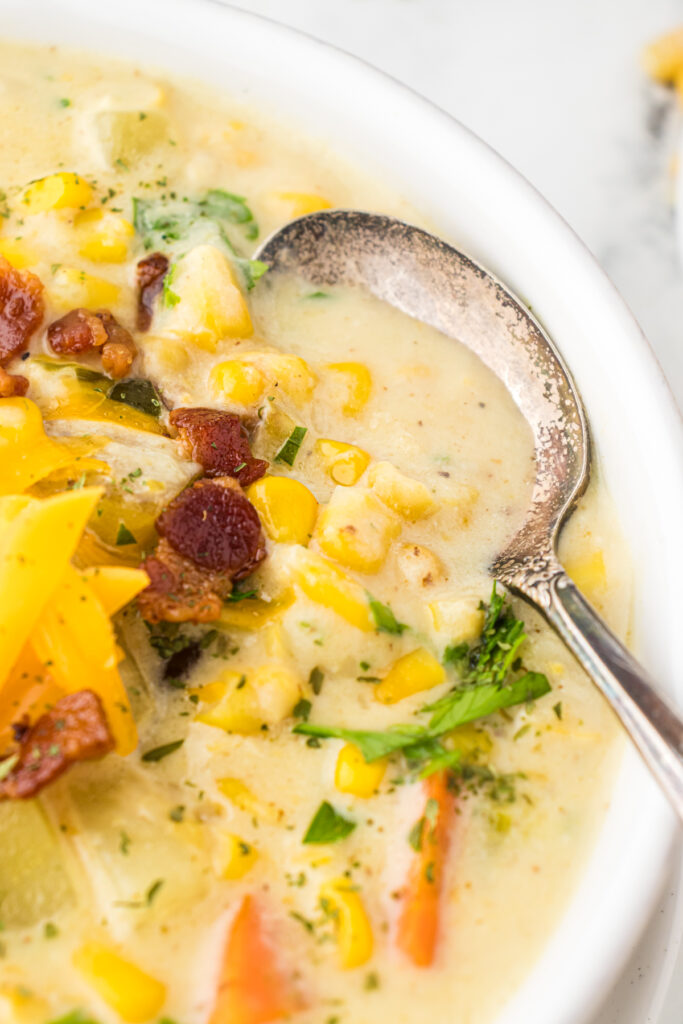 Bowl of hearty, creamy corn chowder featuring fresh corn, yukon gold potatoes, carrots, leeks, bacon, and fresh parsley.